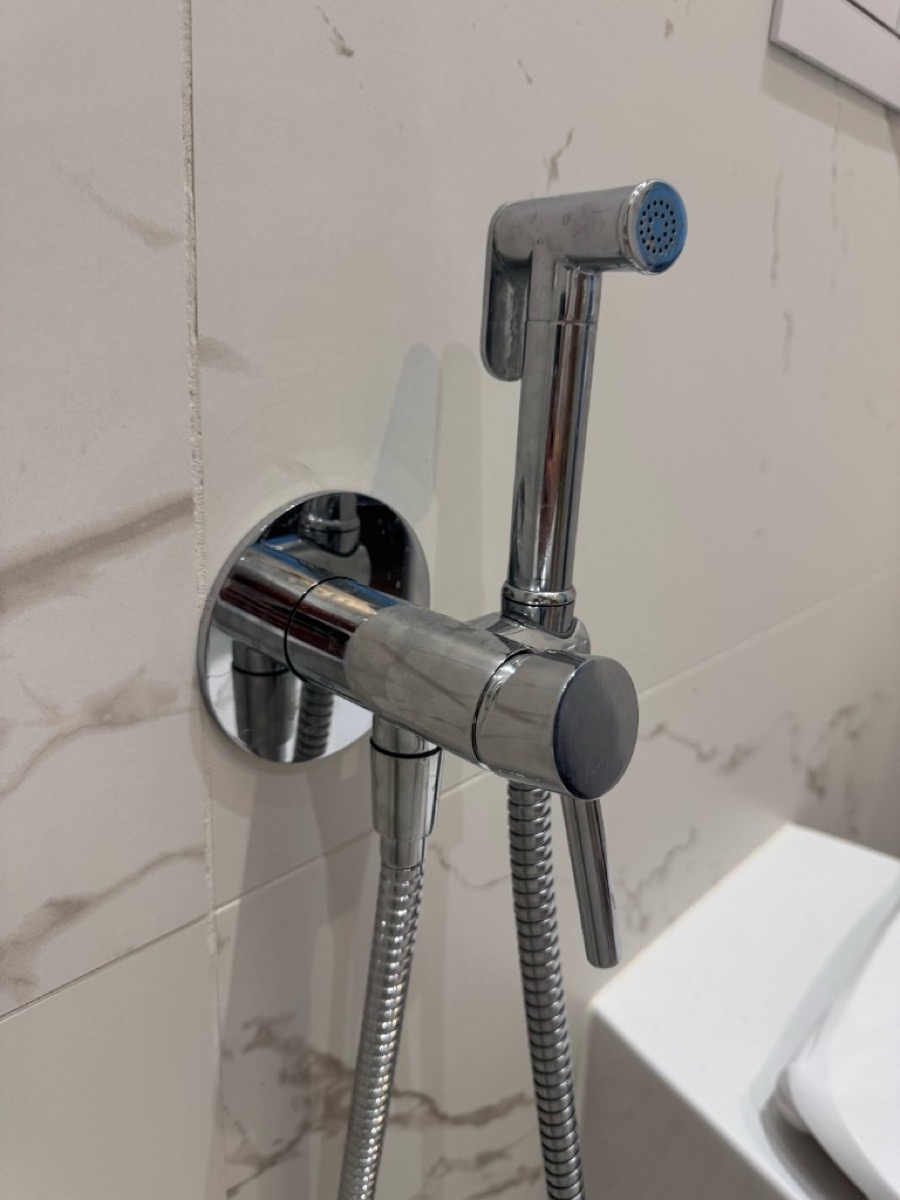 Close-up of chrome hygienic shower handset in its wall cradle with coiled hose