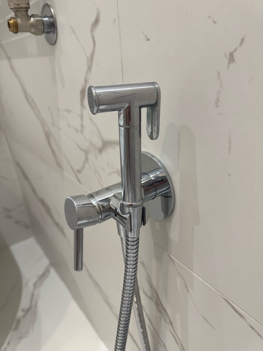 Chrome wall mixer and hygienic shower cradle with coiled hose on marble tiles
